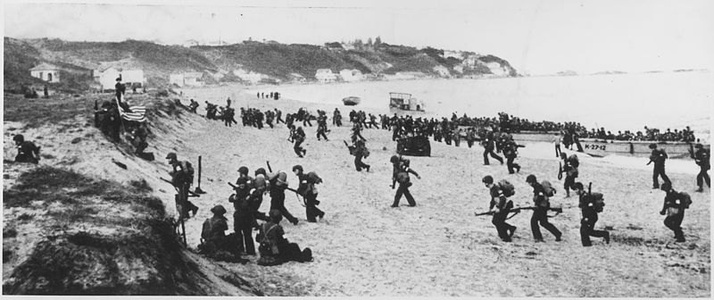 Near Algiers, "Torch" troops hit the beaches behind a large American flag "Left" hoping for the French Army not fire on it.
