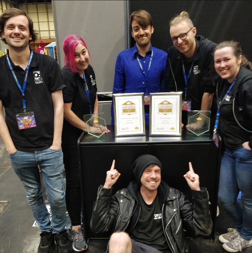 A photo of the Osprey Games team smiling standing around the UKGE 2022 awards we won