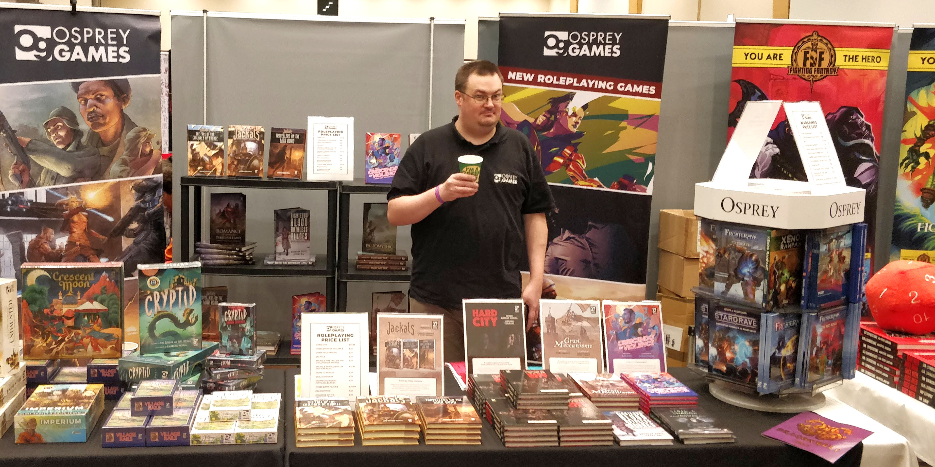 A photo of a member of the Osprey Games team stood behind our stand at Dragonmeet 2022