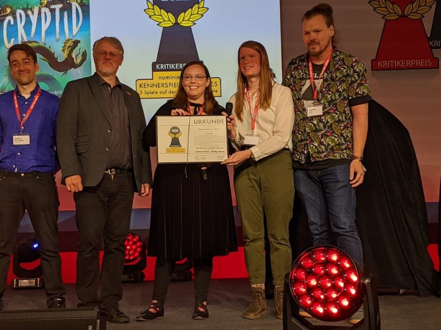 A photo of a member of Osprey Games and Skellig Games with the designers of Cryptid receiving their official certificate for the game's Spiel Des Jahres 2022 Shortlist nomination